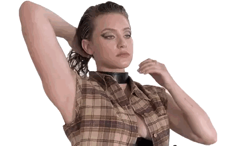 a woman wearing a plaid shirt and a black choker adjusts her hair