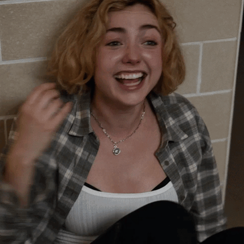 A Woman Wearing A Plaid Shirt And A White Tank Top Smiles GIF