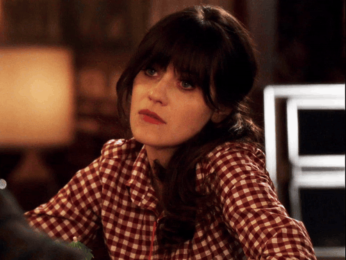 A Woman Wearing A Plaid Shirt Is Looking At Something GIF