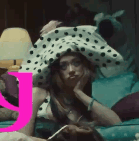 A Woman Wearing A Polka Dot Hat Is Laying On A Bed . GIF
