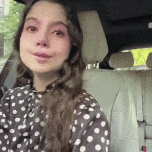 A Woman Wearing A Polka Dot Shirt Is Sitting In The Back Seat Of A Car GIF