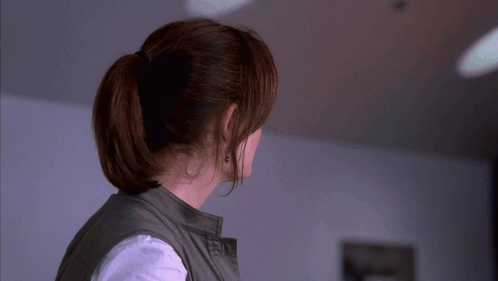 A Woman Wearing A Ponytail And Earrings Looks To The Side GIF