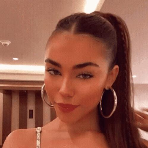 A Woman Wearing A Ponytail And Hoop Earrings Looks At The Camera GIF