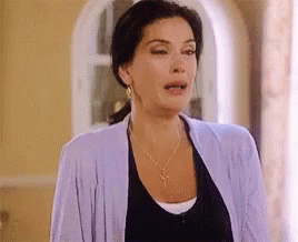 A Woman Wearing A Purple Cardigan And A Black Shirt Is Standing In A Room . GIF