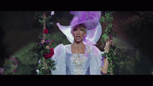A Woman Wearing A Purple Hat And A White Dress Is Standing On A Swing GIF