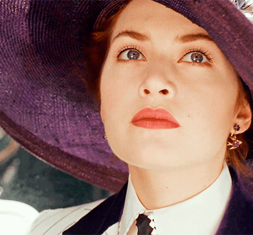 A Woman Wearing A Purple Hat And Earrings Looks Up At Something GIF