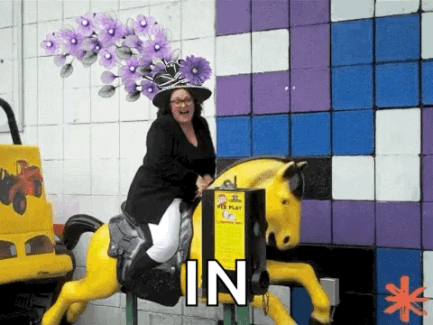 A Woman Wearing A Purple Hat Is Riding A Carousel Horse . GIF