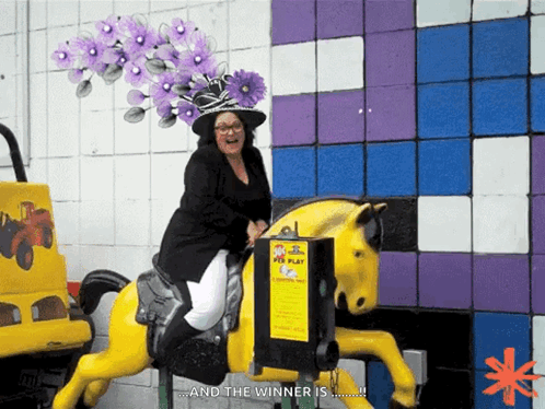 A Woman Wearing A Purple Hat Is Riding A Yellow Horse That Says And The Winner Is GIF