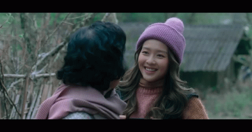 A Woman Wearing A Purple Hat Is Smiling At Another Woman In A Pink Sweater GIF
