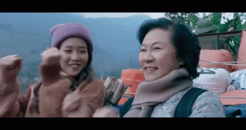 A Woman Wearing A Purple Hat Is Standing Next To An Older Woman Wearing A Sweater And Scarf . GIF