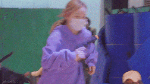 a woman wearing a purple hoodie and a white mask is holding a toy .