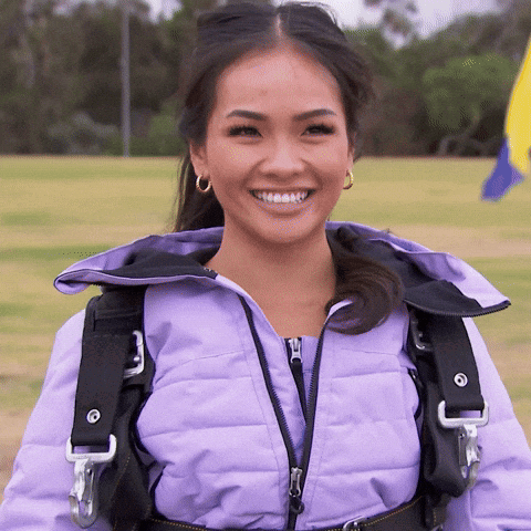 A Woman Wearing A Purple Jacket And A Black Harness Smiles GIF