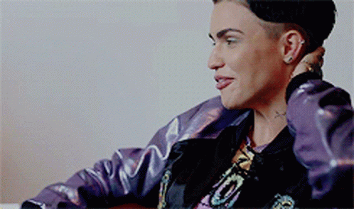 A Woman Wearing A Purple Jacket And A Black Hat Is Sitting In A Chair GIF