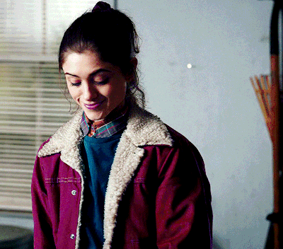 A Woman Wearing A Purple Jacket And A Plaid Shirt Smiles GIF