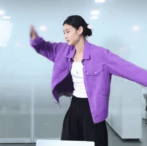 A Woman Wearing A Purple Jacket And A White Tank Top Is Dancing . GIF