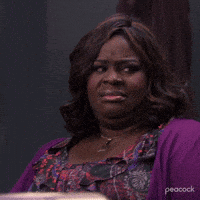 A Woman Wearing A Purple Sweater And A Floral Dress Is Making A Face . GIF