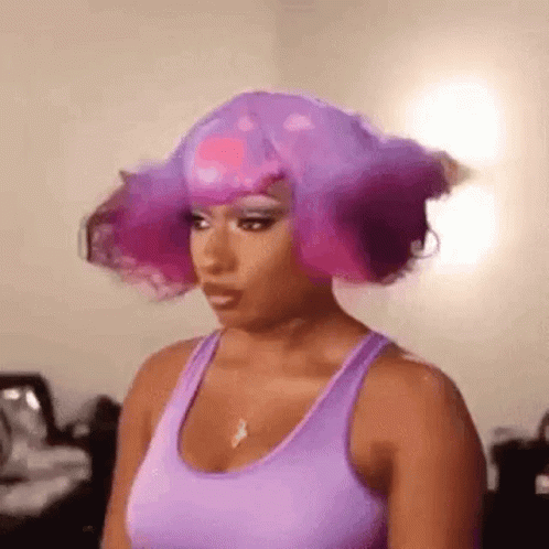 a woman wearing a purple tank top and a purple wig is standing in a room .