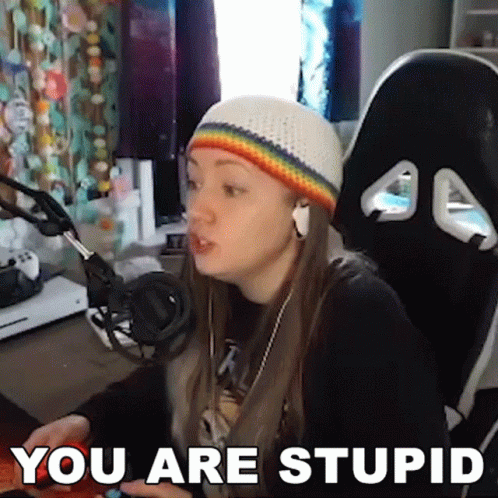 A Woman Wearing A Rainbow Hat And Headphones Is Sitting In Front Of A Computer With The Words " You Are Stupid " Above H GIF