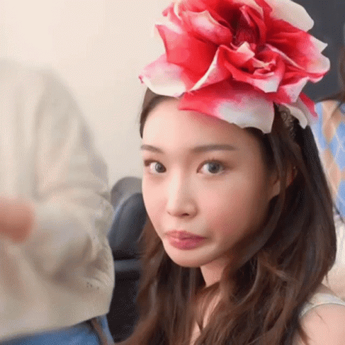 A Woman Wearing A Red And White Flower On Her Head Making A Face GIF