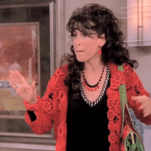 A Woman Wearing A Red Cardigan And A Black Shirt Is Waving . GIF