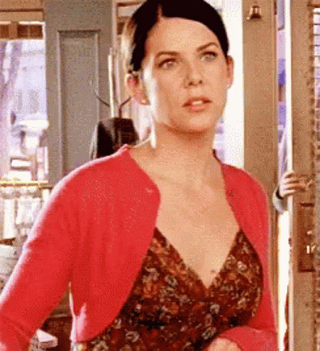 A Woman Wearing A Red Cardigan And A Floral Dress Is Standing In A Doorway . GIF