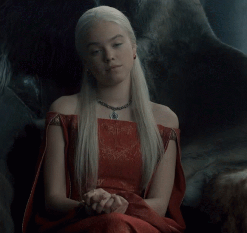 A Woman Wearing A Red Dress And A Necklace Sits In A Chair GIF
