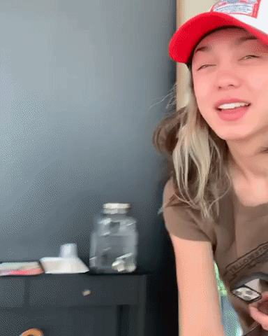 A Woman Wearing A Red Hat And A Brown Shirt Is Holding A Cell Phone . GIF