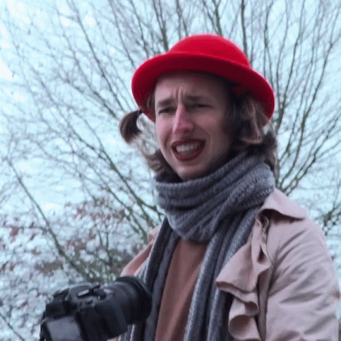 A Woman Wearing A Red Hat And A Scarf Holds A Camera GIF