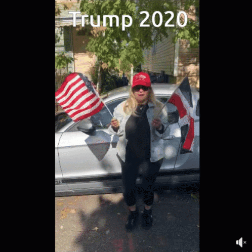 A Woman Wearing A Red Hat That Says Trump 2020 Stands In Front Of A Silver Car GIF