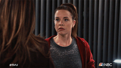 A Woman Wearing A Red Hoodie Is Sitting In Front Of A Curtain With Nbc Written On It GIF