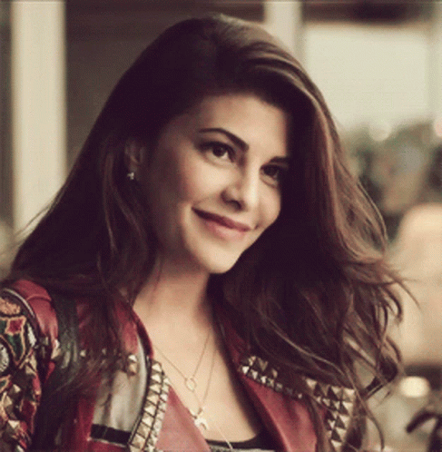 A Woman Wearing A Red Jacket And A Necklace Is Smiling For The Camera GIF