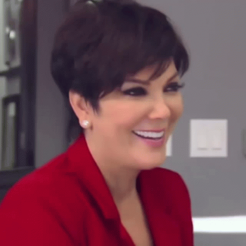 A Woman Wearing A Red Jacket And Earrings Is Smiling And Looking At The Camera . GIF