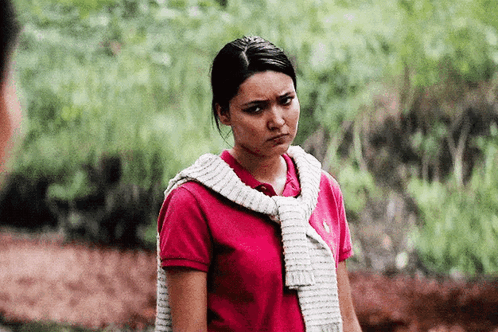 A Woman Wearing A Red Polo Shirt And A White Sweater Around Her Neck Is Making A Funny Face . GIF