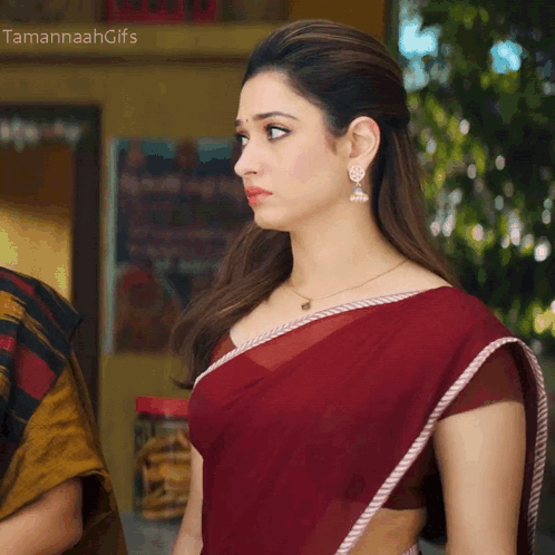A Woman Wearing A Red Saree And Earrings Stands In Front Of A Sign That Says " Tamannahgifs " GIF