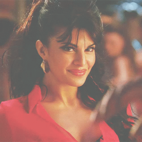 A Woman Wearing A Red Shirt And Earrings Smiles GIF