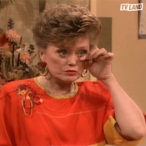A Woman Wearing A Red Shirt And Earrings Wipes Her Eyes With Her Hand .. GIF
