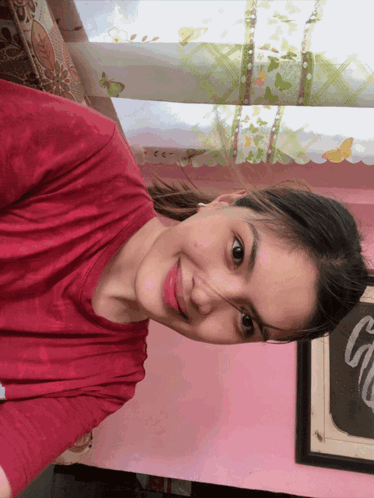a woman wearing a red shirt is smiling in front of a pink wall