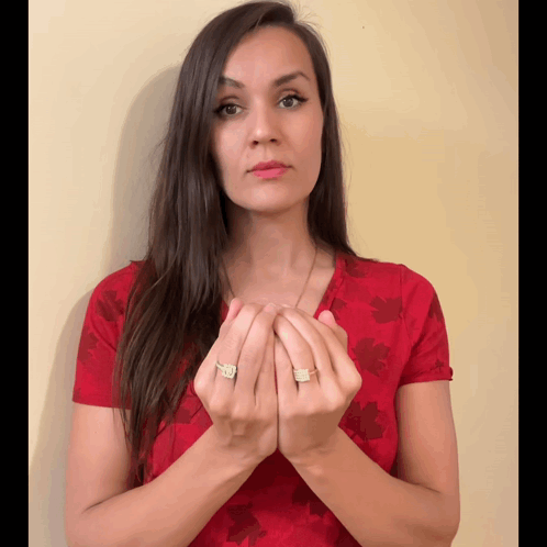 A Woman Wearing A Red Shirt With A Maple Leaf Pattern Holds Her Hands Together GIF