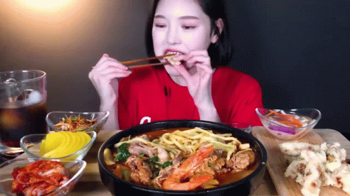 A Woman Wearing A Red Shirt With The Letter C On It Is Eating Noodles With Chopsticks GIF