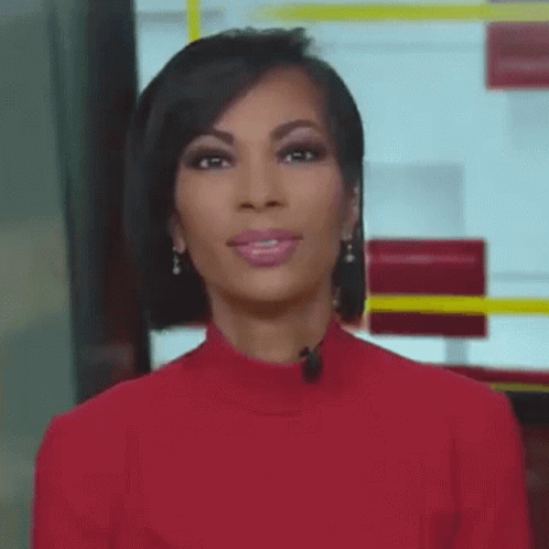 A Woman Wearing A Red Sweater And Earrings Is Standing In Front Of A Microphone . GIF