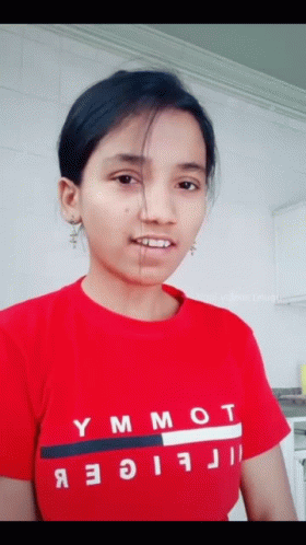 A Woman Wearing A Red Tommy Hilfiger Shirt Looks At The Camera GIF