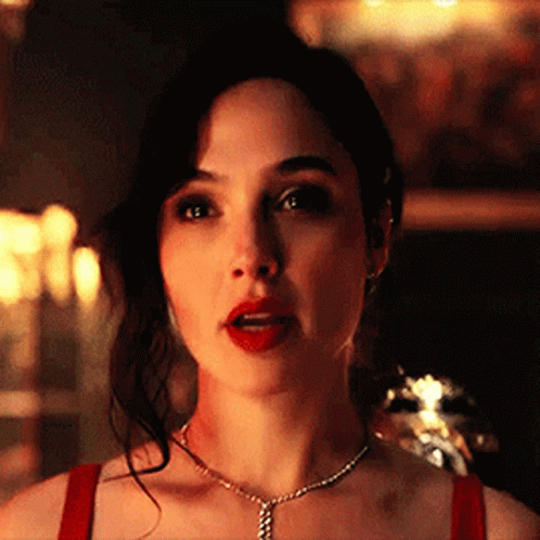 A Woman Wearing A Red Top And A Necklace Is Looking At The Camera . GIF