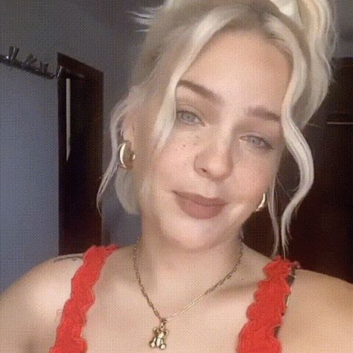 A Woman Wearing A Red Top And A Necklace With A Teddy Bear Pendant . GIF
