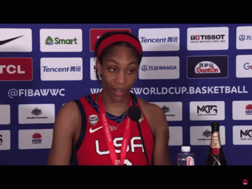 A Woman Wearing A Red Usa Jersey Stands In Front Of A Tcl Advertisement GIF