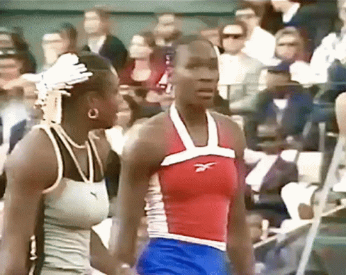 A Woman Wearing A Red White And Blue Reebok Tank Top Stands Next To Another Woman GIF