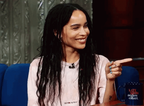 A Woman Wearing A Saint Laurent Shirt Is Smiling And Pointing At Something GIF