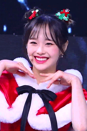 A Woman Wearing A Santa Costume Is Smiling And Making A Heart Shape With Her Hands GIF