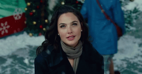 A Woman Wearing A Scarf And A Coat Is Standing In Front Of A Christmas Tree . GIF
