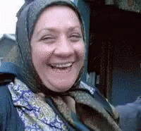 A Woman Wearing A Scarf And A Head Scarf Is Smiling For The Camera . GIF
