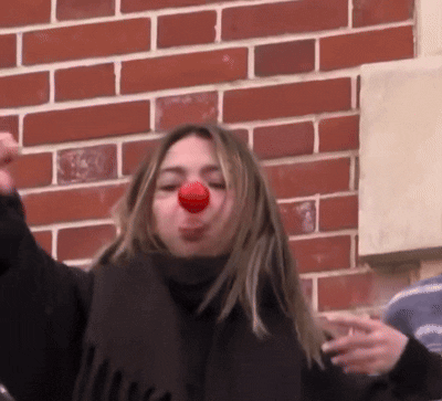 Woman With Scarf And Red Nose In Front Of Brick Wall GIF